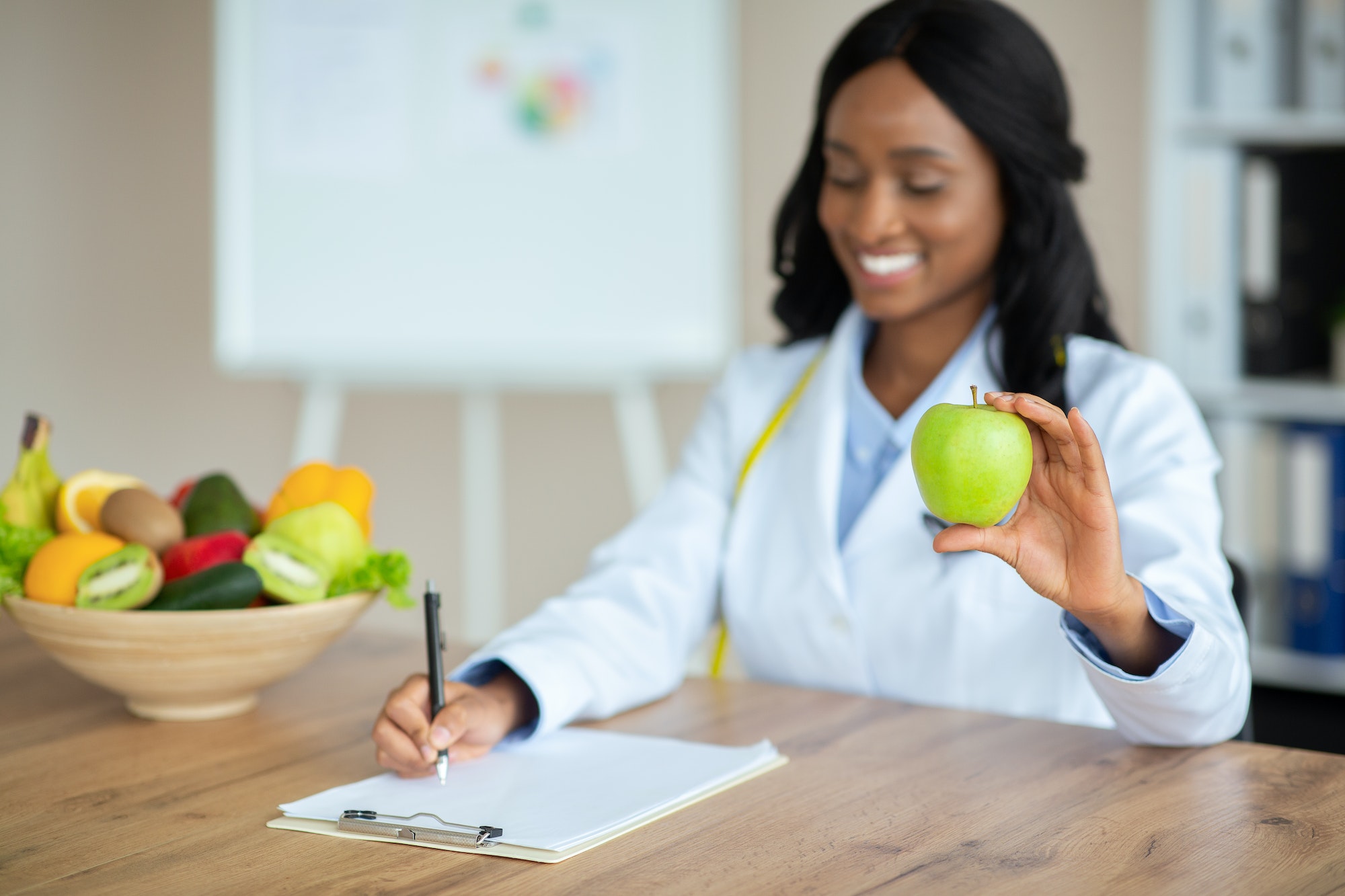 Cheerful African American nutrition adviser planning meals for client at clinic, copy space